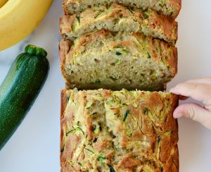 A sliced loaf of Zucchini Banana Bread with a child's hand touching it