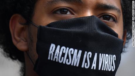 A protester wears a protective face covering with the slogan &quot;Racism is a Virus&quot; written on the fabric as he listens to speeches at a gathering in support of the Black Lives Matter movement at Marble Arch in London on July 5, 2020, in the aftermath of the death of unarmed black man George Floyd in police custody in the US. (Photo by JUSTIN TALLIS / AFP) (Photo by JUSTIN TALLIS/AFP via Getty Images)