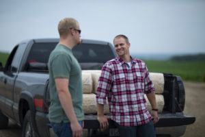 Two farmers chatting near a truck filled with hay.